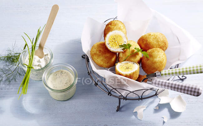Huevos empanados en papel pergamino en una canasta metálica junto a una salsa de mostaza y remoulade - foto de stock