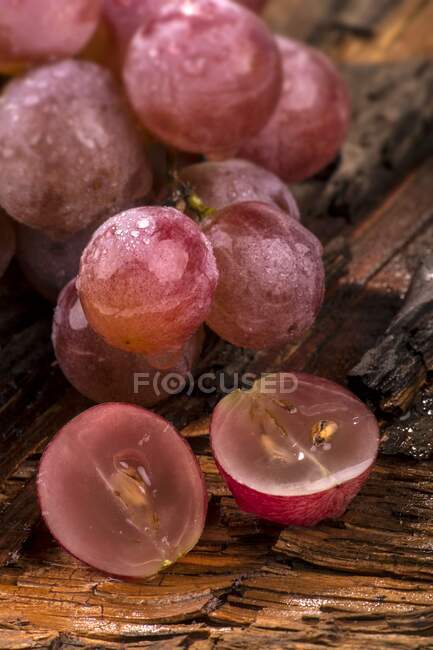 Uvas rojas con gotitas de agua, una a la mitad - foto de stock