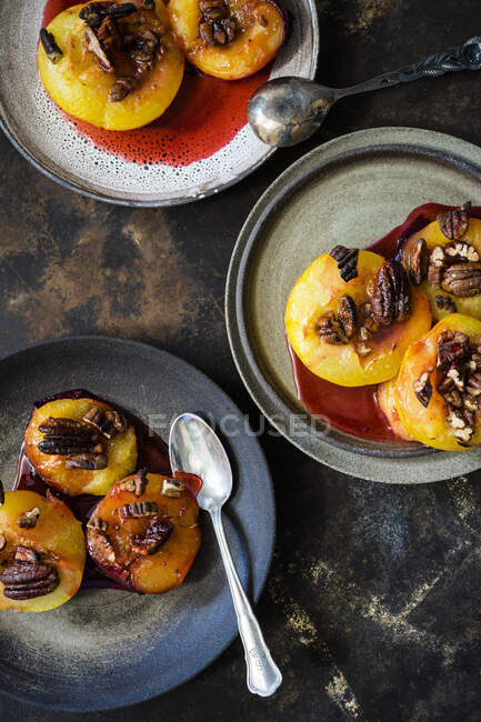 Caramelized plums with pecan nuts on plates with spoons — Stock Photo