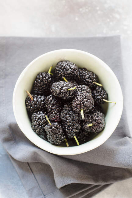 Fresh mulberries in small ceramic bowl on gray cloth — Stock Photo