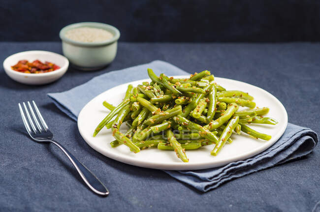Plate of stir fried green beans with sesame seeds on a blue background — Stock Photo