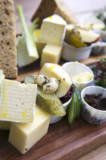 A cheese platter featuring pickled vegetables, fruit and bread — Stock Photo