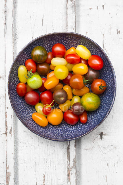 Fresh red and yellow tomatoes in a bowl on a wooden background — Stock Photo