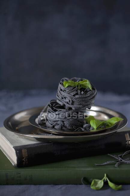 Black ribbon noodles and basil leaves on metal plate — Stock Photo