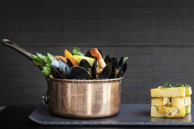 A copper saucepan of mussels with prawns, corn and vegetables served with a stack of chunky chips — Stock Photo
