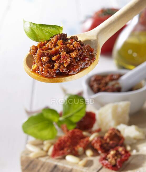 Tomatenpesto und Basilikumblätter auf einem Holzlöffel über einem Holzbrett mit Basilikum und getrockneten Tomaten — Stockfoto