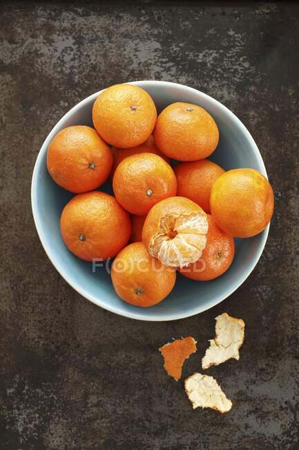 Mandarinas, inteiras e descascadas na tigela e na superfície metálica — Fotografia de Stock