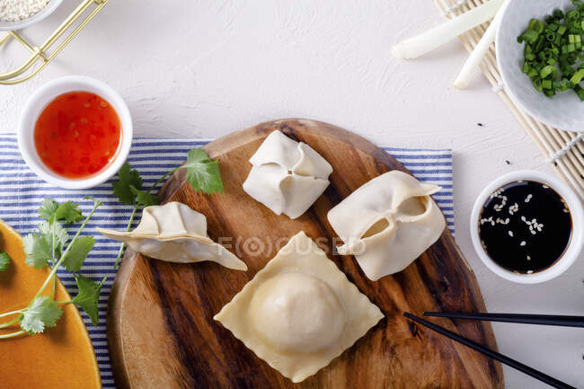 Various raw dumplings on a wooden board next to two sauces — Stock Photo