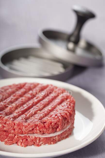 Two hamburgers with a hamburger press in the background — Stock Photo