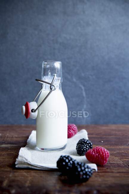 Garrafa de leite com framboesas frescas e amoras na mesa de madeira — Fotografia de Stock
