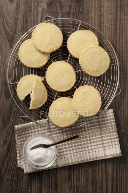 Shortbreads on cooling rack and bowl on sugar with spoon — Stock Photo