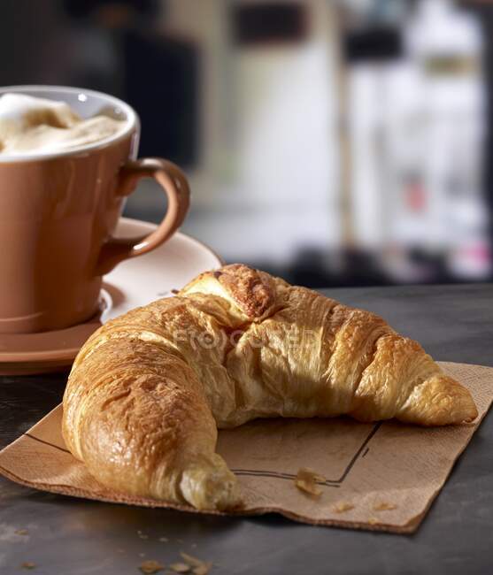 Un croissant con un café con leche en un café - foto de stock