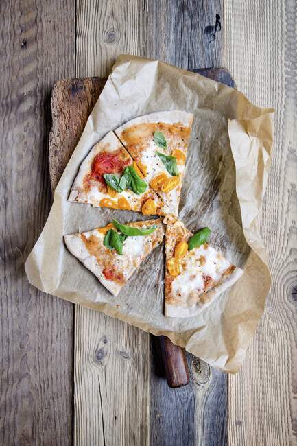 Pizza with mozzarella, tomatoes and basil on baking paper — Stock Photo