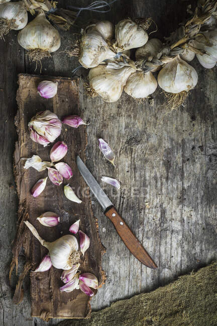 Bulbi di aglio aperti su corteccia di albero e ghirlanda di aglio su superficie rustica di legno — Foto stock