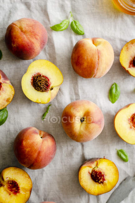 Свежие персики и персиковые половинки на льняной скатерти — стоковое фото