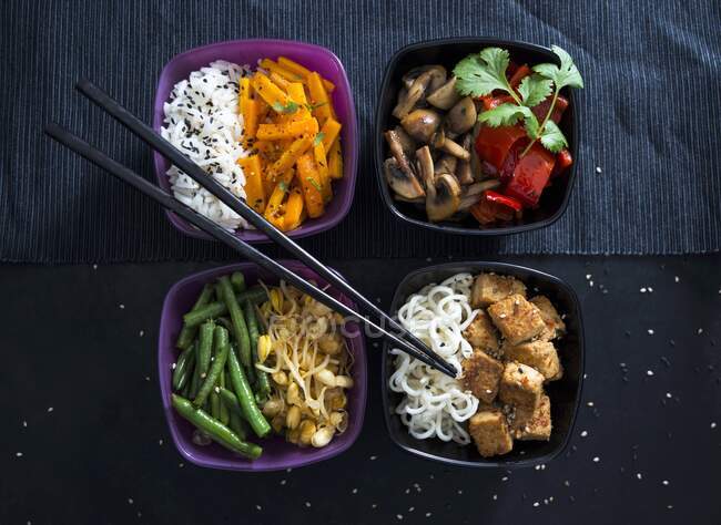 Four bowls with rice, roasted carrots, mushrooms, peppers, beans, mung beans, Mie noodles and tofu (Vegan) — Stock Photo