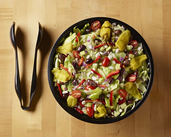 Греческий салат с пластиковыми щипцами на столе мясника сверху — стоковое фото