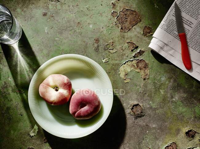 Pfirsiche auf Teller neben Zeitung und Obstmesser — Stockfoto