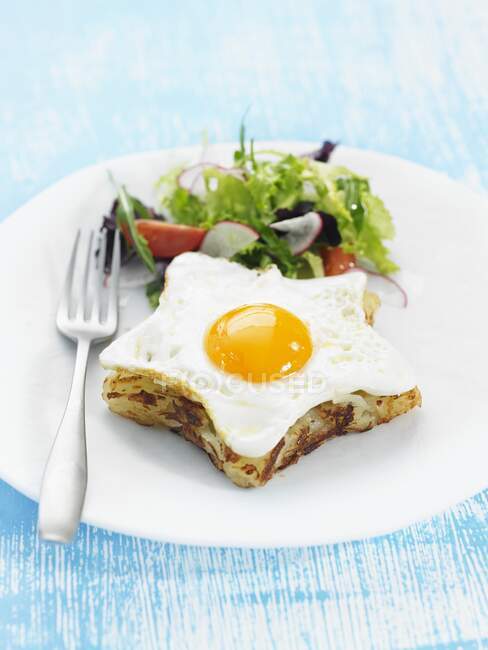 Зіркоподібний іспанський омлет увінчаний смаженим яйцем і бічним салатом. — стокове фото