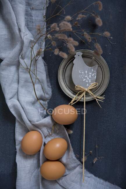 Easter decorations with chicken eggs and a branch beside a chicken motif on a blue background — Stock Photo