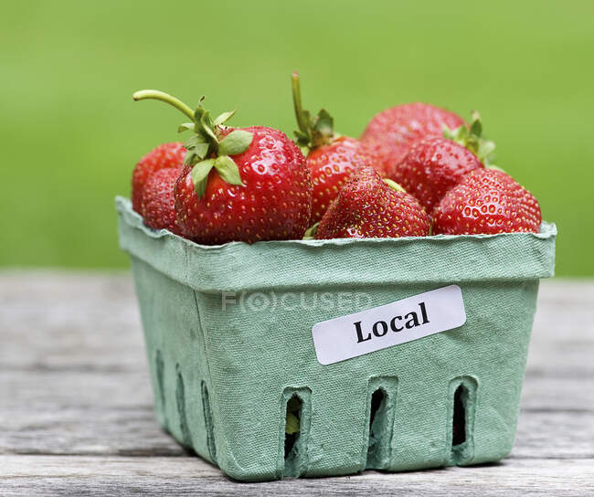 Fresas en un recipiente de papel con una etiqueta de inscripción local - foto de stock