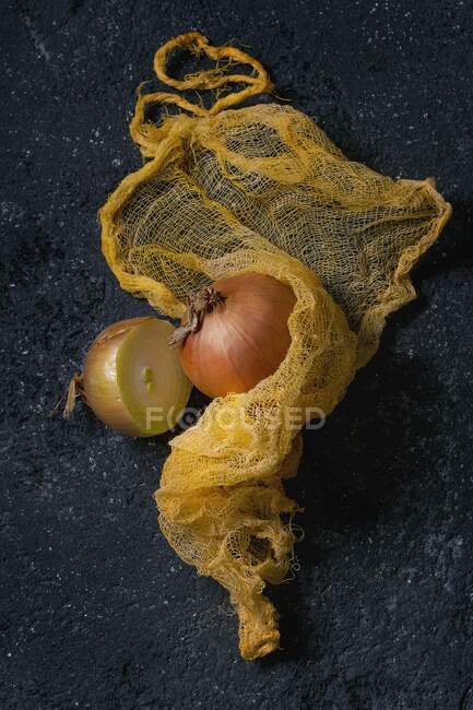 Cebolla entera y la mitad de cebolla amarilla en trapo amarillo sobre fondo de piedra negra - foto de stock