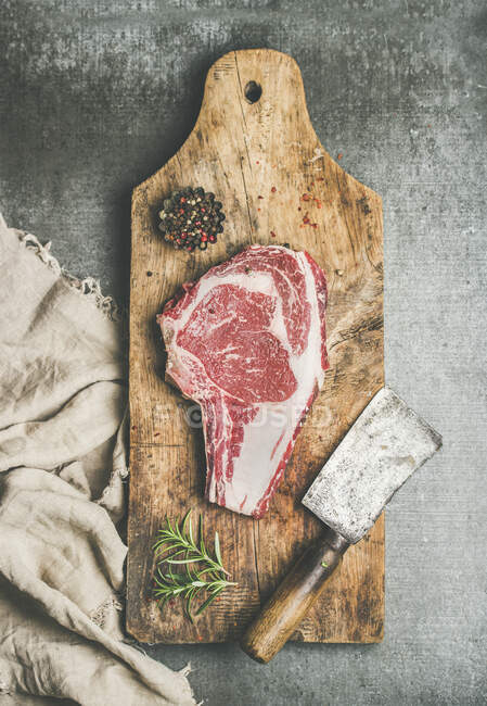 Colocação plana de carne crua de vaca de primeira qualidade bife seco costela olho sobre osso com tempero e faca de helicóptero — Fotografia de Stock