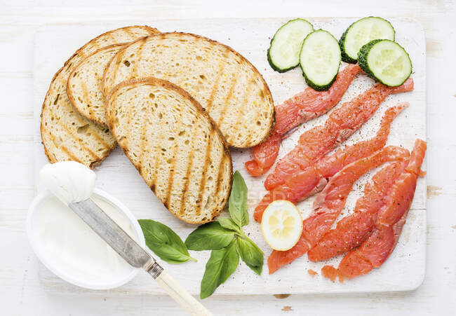 Grilled bread slices, smoked salmon, cottage cheese, cucumber and basil — Stock Photo
