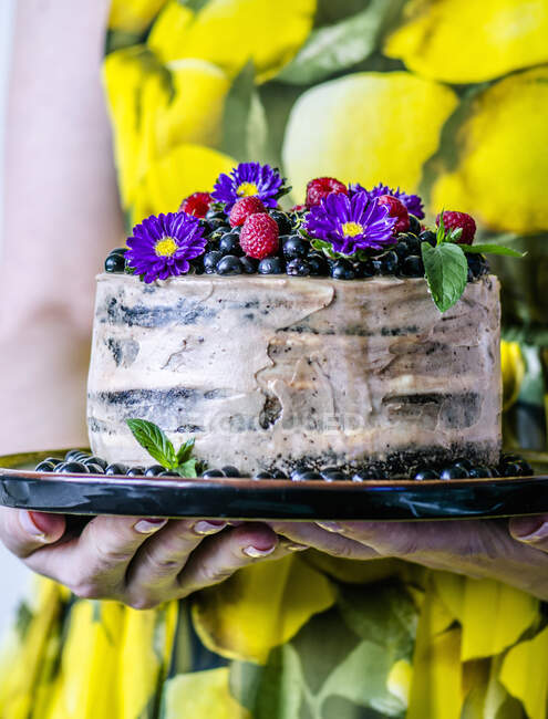 A woman in a yellow dress is holding a cake with bird cherries and flowers — Stock Photo