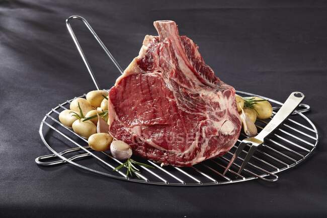Costelas de carne de vaca crua, alho e batatas em uma grade de cozinha — Fotografia de Stock