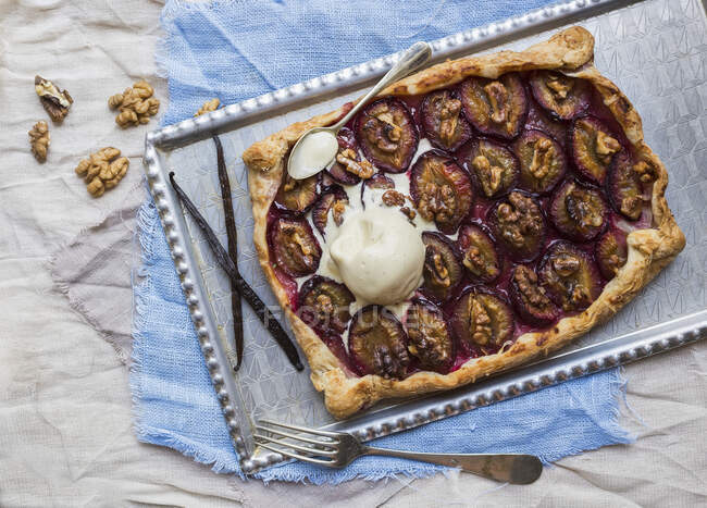 Rustic plum pie with walnuts and ice-cream on a silver tray over pieces of linen fabric — Stock Photo