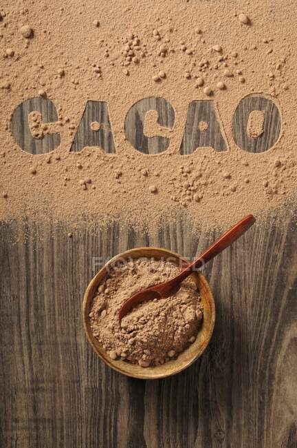 Cocoa powder in a bowl and spilled on a wooden background with the word 'cacao' — Stock Photo