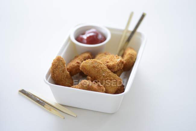 Nuggets de pollo y ketchup en un contenedor para llevar - foto de stock