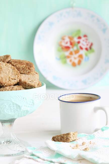 Glass bowl of biscuits with coffee in enamel cup — Photo de stock