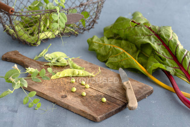 Pea pods on a wooden board next to colourful chard stems — Stock Photo