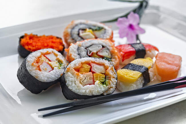 Assortiment de makis et sushis sur plaque blanche avec baguettes — Photo de stock