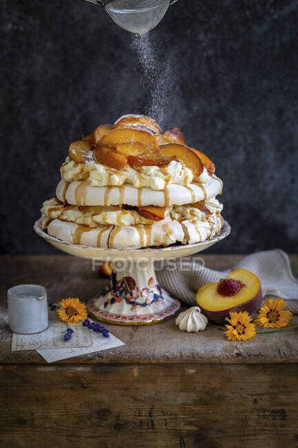 Pavlova cake with peaches, caramel sauce and sifting powdered sugar — Stock Photo