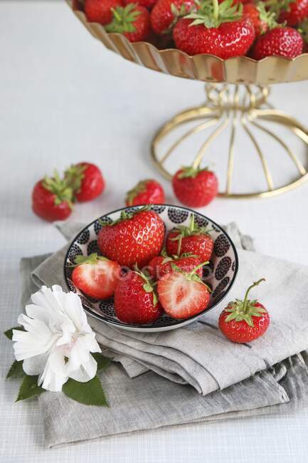 Fresas frescas enteras y cortadas a la mitad en tazón, decoradas con flor de papel - foto de stock