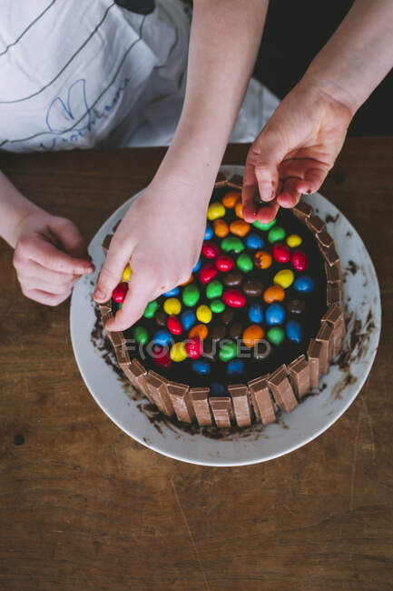 Niños manos decorando un pastel con caramelos de colores - foto de stock
