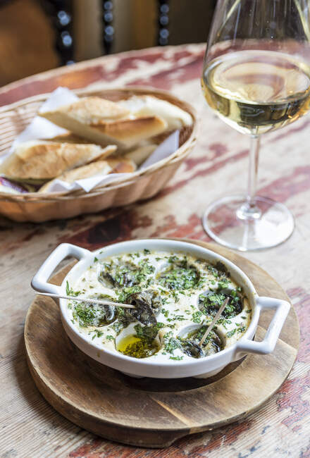Assiette d'escargots français dans une sauce au beurre aux herbes avec du pain et du vin en arrière-plan — Photo de stock
