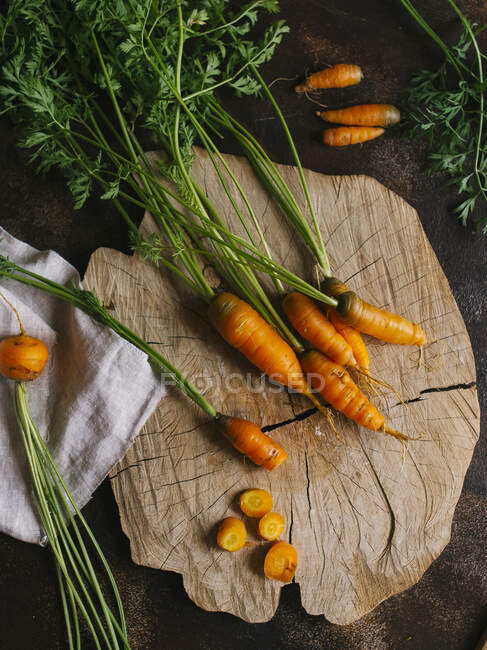 Whole and chopped carrots on wooden surface — Stock Photo