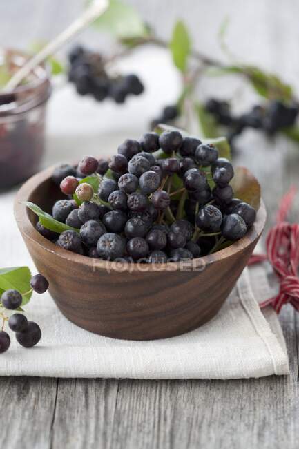 Aronia berries in wooden bowl and on table with green leaves — Stock Photo