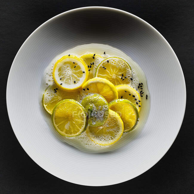 Limones y limas con semillas de sésamo negro y espuma - foto de stock