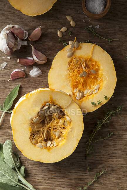 A halved munchkin pumpkin with garlic, sage and thyme on a wooden background — Stock Photo