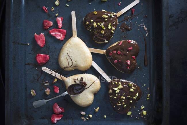 Herzförmige vegane Kuchen auf Sticks, dekoriert mit dunkler Bierglasur, gefriergetrockneten Erdbeeren und Pistazien — Stockfoto