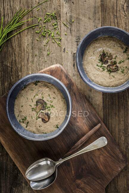 Zwei Schüsseln mit dicker und cremiger Pilzsuppe garniert mit Pilzscheiben und Schnittlauch in blauen Schüsseln auf einer Holzoberfläche — Stockfoto