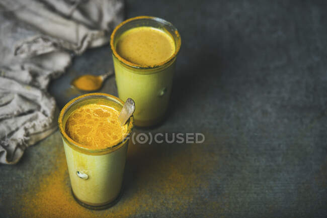 Golden milk with turmeric powder in glasses over dark grunge background — Stock Photo