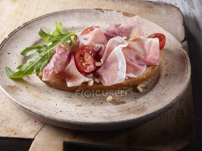 Une tranche de pain garnie de jambon toscan, tomates et fusée — Photo de stock