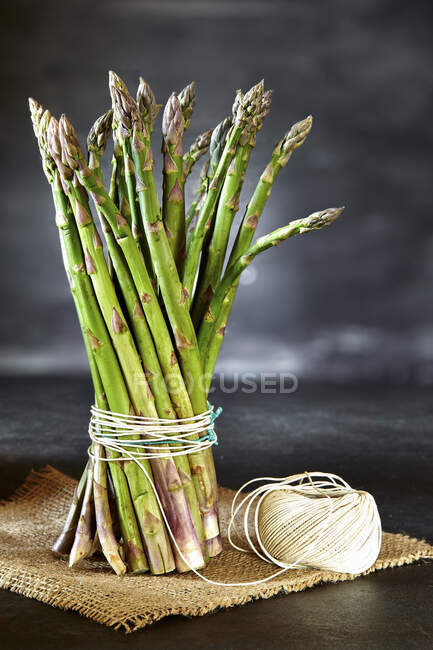Bando de espargos amarrados com fio de cozinha, em um pedaço de saco de cânhamo — Fotografia de Stock