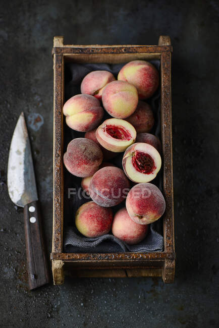 Свіжі маленькі персики в дерев'яній коробці і ножі — стокове фото